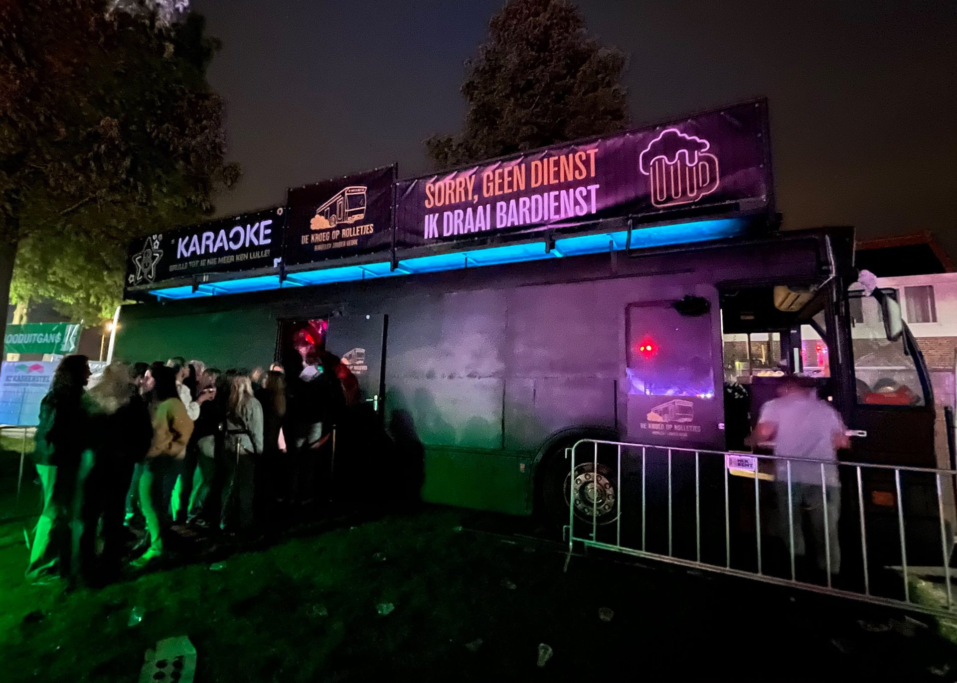 Rij gasten bij de ingang van de bus in de avond met neonverlichting.