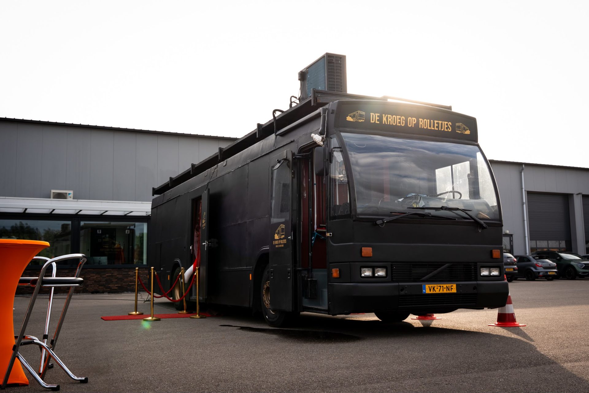 De Kroegbus buiten bij zonsondergang met rode loper.