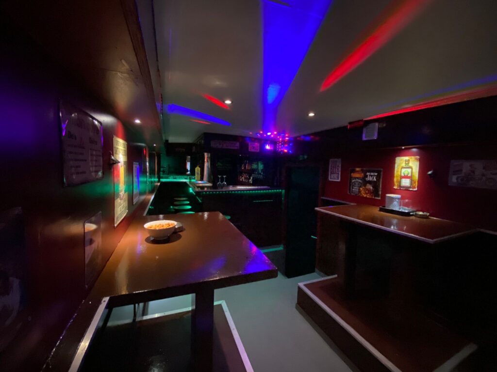 De bar in de bus met bierflesjes, rood licht en oude reclameborden.
