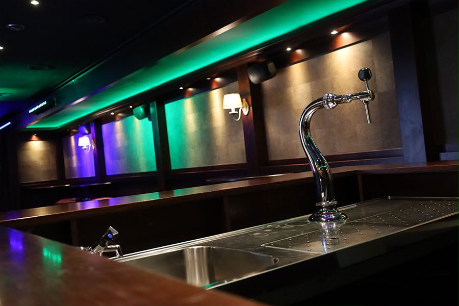 De bar van De Kroeg XL met chromen tapkraan en groen-paarse sfeerverlichting.
