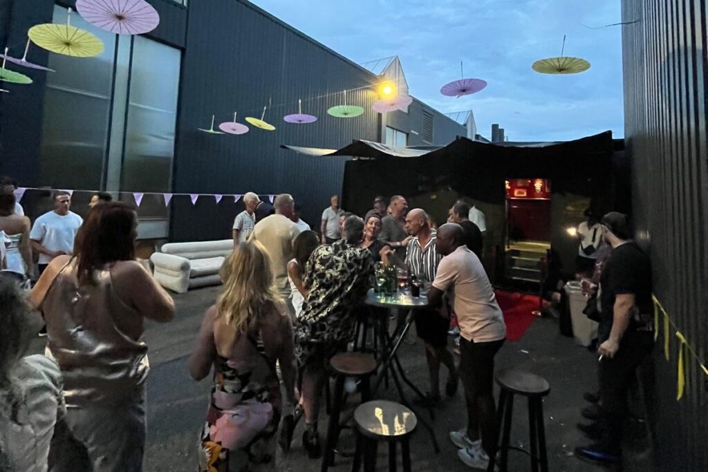 Feest buiten de bus met statafels en parasols in de schemering.