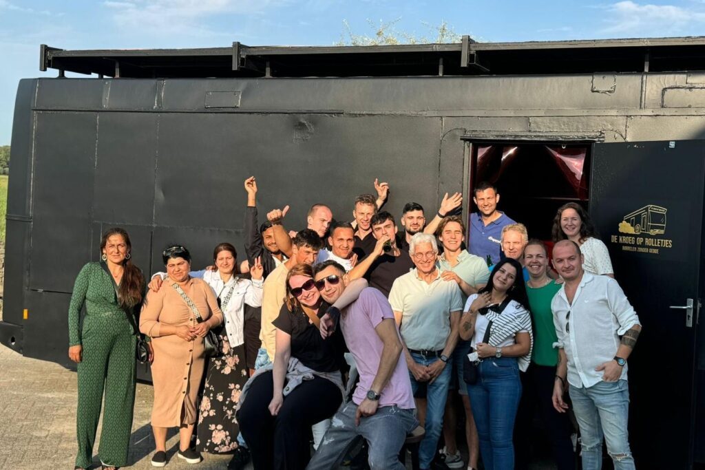 Groep gasten voor de bus tijdens een borrel in de buitenlucht.