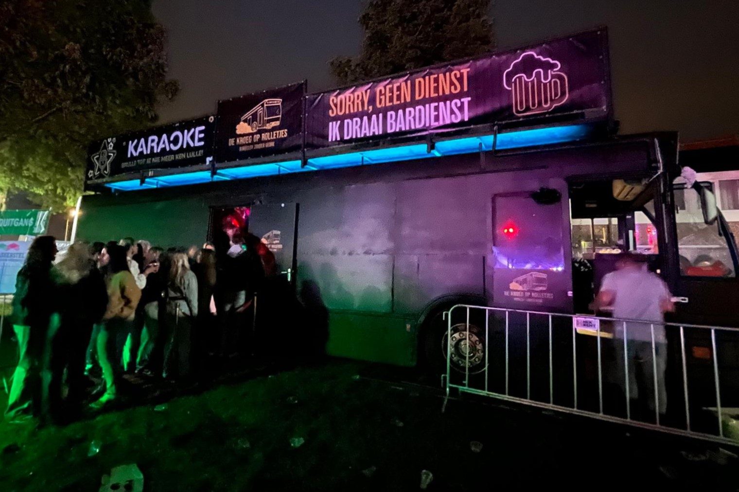 De bus op een evenement in de avond met publiek en verlichte banners.