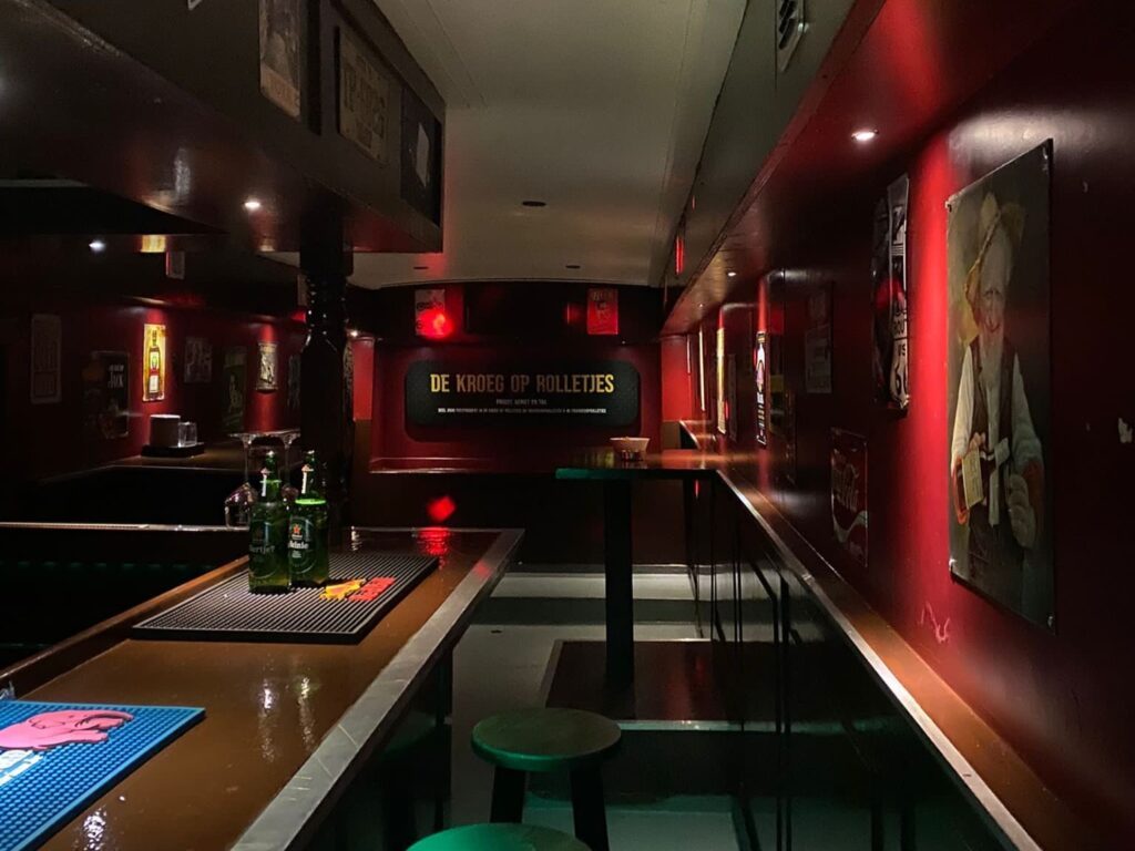 Het interieur van de kroeg met rode wanden, statafels en biertjes op de bar.
